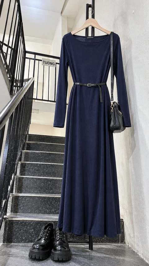 A belted navy long-sleeve dress hangs beside a stair railing, accompanied by a black bag and dark lace-up boots.